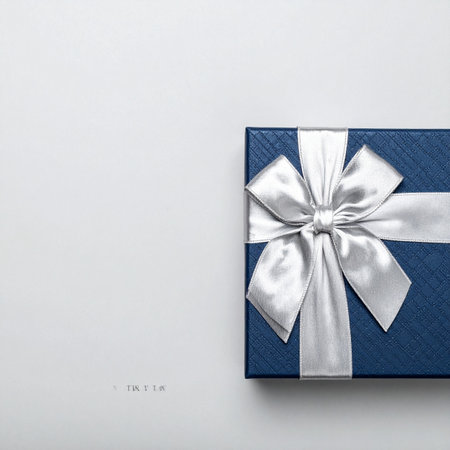 A beautifully wrapped blue gift box, tied with a luxurious silver satin ribbon, sits against a clean, minimalist background.の素材
