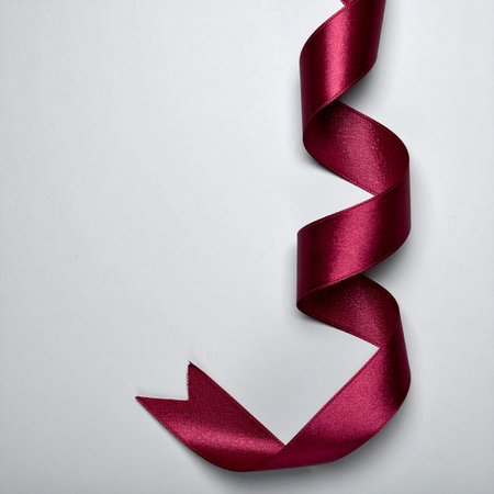 A single, luxurious burgundy satin ribbon unfurls in a graceful, twisting spiral against a clean, minimalist background.の素材