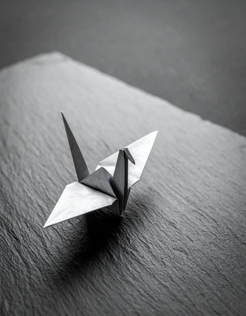 A single, meticulously folded origami crane rests on a dark, textured surface.の素材