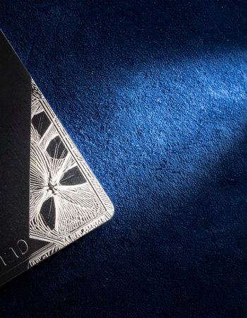 In a dramatic beam of light, the corner of an exclusive, engraved metal card is revealed against a deep blue textured surface.の素材