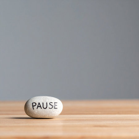 In a quiet, minimalist space, a smooth stone rests on a wooden surface, carrying a single, powerful word: PAUSE.の素材