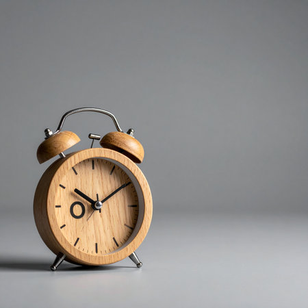 A classic wooden alarm clock stands against a clean, gray background.の素材