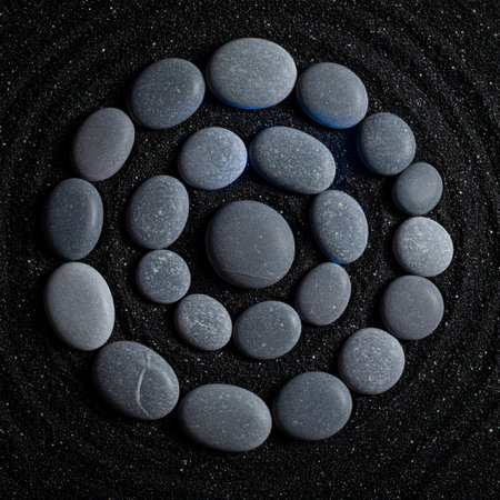 A carefully arranged spiral of smooth gray stones rests on a bed of fine black sand.の素材