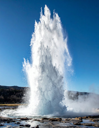 A spectacular display of nature's raw power as a geyser erupts, sending a massive column of boiling water and steam high into the crisp, blue sky.の素材