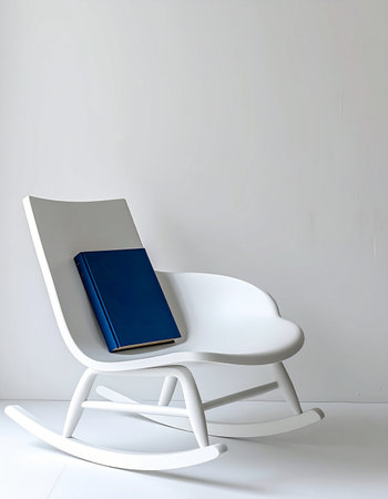 A single blue book rests on a clean, white rocking chair, waiting for a reader. This minimalist scene evokes a sense of peace, quiet contemplation, and the simple joy of escaping into a good story.の素材