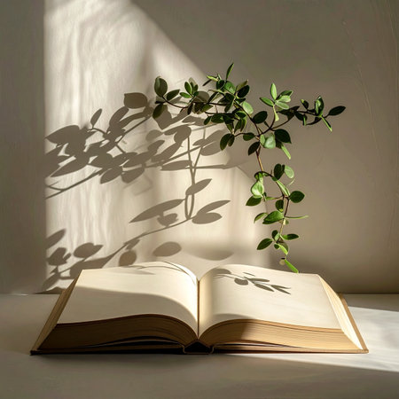 Golden morning light streams into a quiet room, casting delicate shadows of a leafy vine across the wall and the open pages of a book.の素材