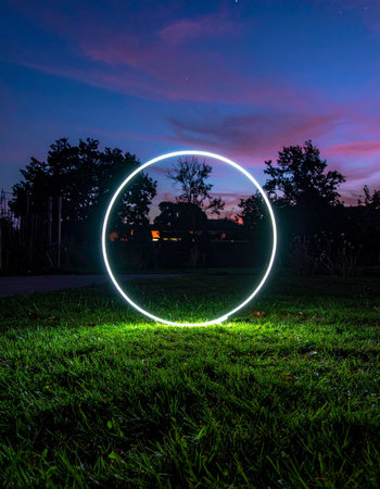 A luminous ring of light hovers mysteriously in a grassy field as twilight paints the sky in shades of purple and orange.の素材