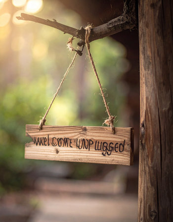 A hand-carved wooden sign hangs from a branch, its 'welcome' message warmed by the golden glow of the sun.の素材