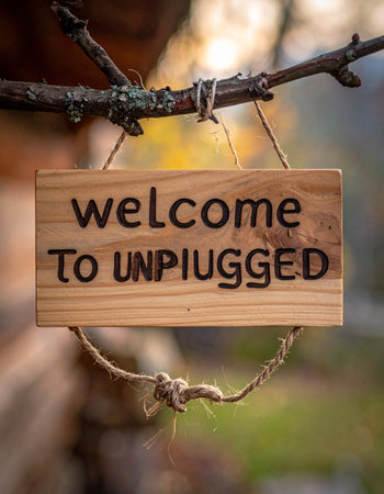 A rustic wooden sign with the words 'Welcome to Unplugged' hangs from a tree branch, inviting visitors to a peaceful retreat.の素材