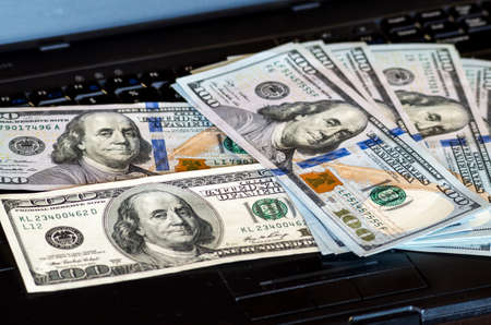 Bunch of dollar bill notes thrown on a laptop keyboard featured defocused bokeh