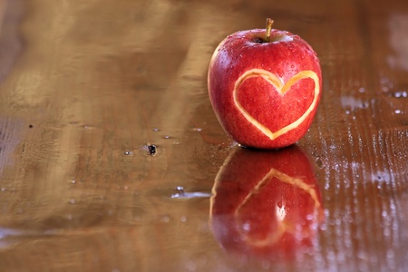 Red wet apple with heart shape on wooden deskの写真素材
