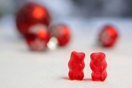 Two red gummy bears with red baubles on a white table clothの写真素材