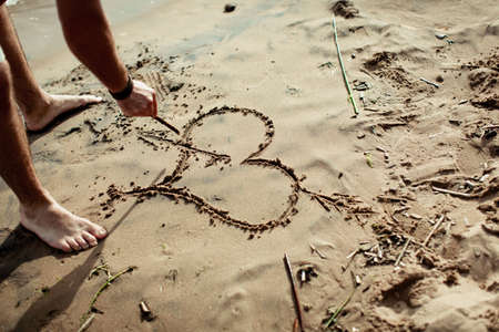 Young beautiful couple on the beach making heartの写真素材