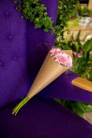 Bouquet of pink gerbera wrapped in craft paper lying on a chairの写真素材