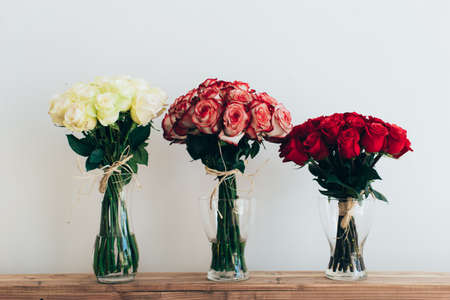 Bouquets of roses in three glass vases next to a watering can on a white wallの写真素材