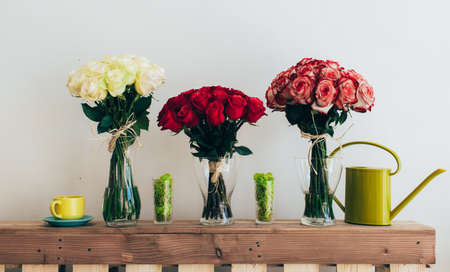 Bouquets of roses in three glass vases next to a watering can on a white wallの写真素材