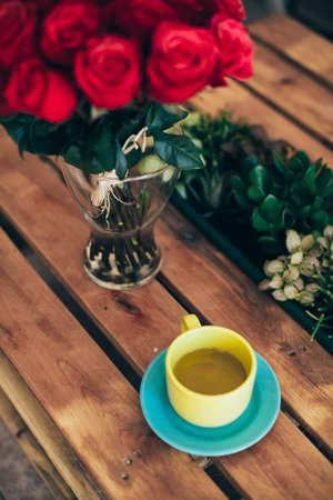 Cup of green tea and a bouquet of roses on a wooden tableの写真素材