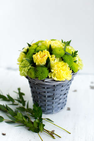 Beautiful bouquet of yellow carnation in basket on bright backgroundの写真素材