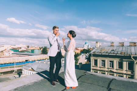 Young couple standing on the roof of the newly-married couple with glasses of champagne in their handsの写真素材