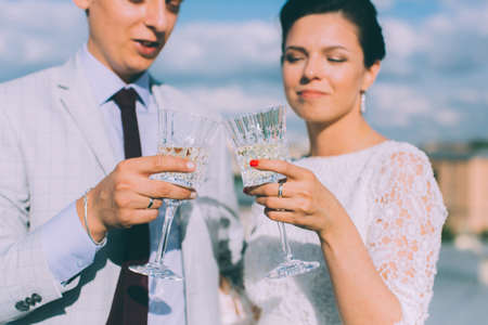 Young couple standing on the roof of the newly-married couple with glasses of champagne in their handsの写真素材