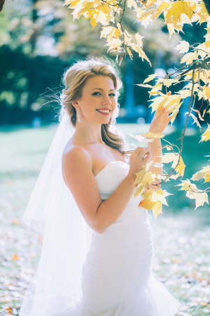 delicate beautiful bride with a white dress against the background of the autumn landscapeの写真素材