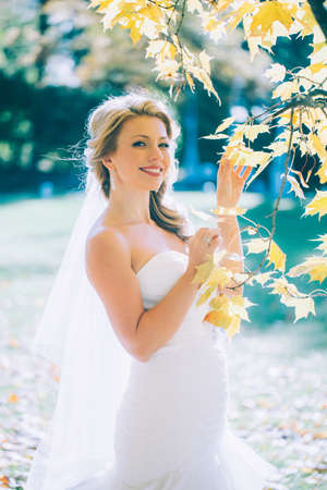delicate beautiful bride with a white dress against the background of the autumn landscapeの写真素材