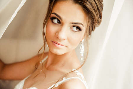 Beautiful happy bride in white silk lingerie in her bedroom in a morningの写真素材