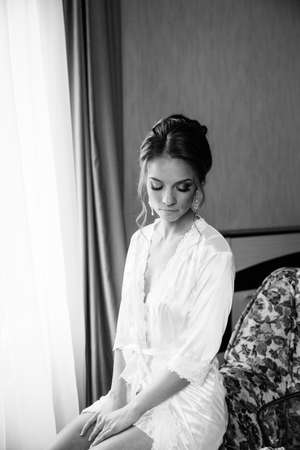 Beautiful happy bride in white silk lingerie in her bedroom in a morningの写真素材