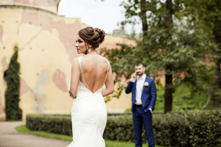 portrait of a beautiful happy brunette bride in wedding white dress holding hands in bouquet of flowers outdoors on the background of green leavesの写真素材