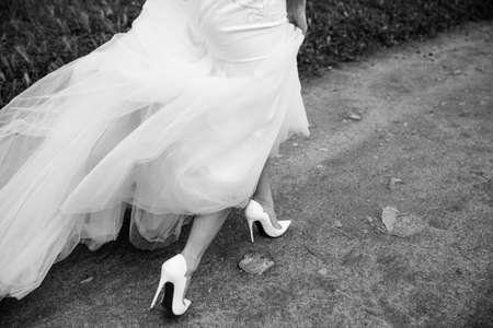 Beautiful bride's shoes with long legs in white wedding dressの写真素材