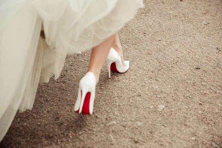 Beautiful bride's shoes with long legs in white wedding dressの写真素材