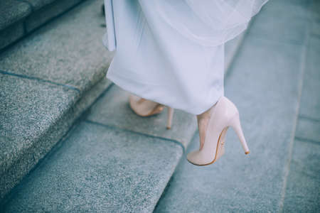 Beautiful bride's shoes with long legs in white wedding dressの写真素材