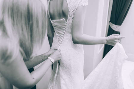 Bridesmaid makes bow-knot on the back of brides wedding dressの写真素材
