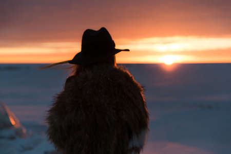 Elegant girl in fur coat and hat at sunset against frozen seaの写真素材