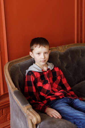 Boy in a plaid shirt with a hood and jeans on a background of an orange wallの写真素材