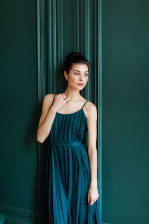Young brunette girl in a green dress on a background of green wall