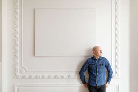 Portrait of a bald brutal Man in jeans standing against a white wallの写真素材