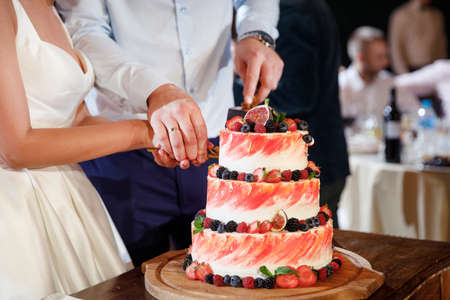 bride and groom cut wedding cake with many different fruits and wild berries and figs on topの写真素材