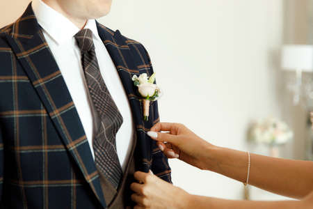 brides hand putting the boutonniere flower on a groom