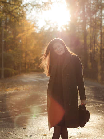 Young beautiful pregnant woman with dark hair in a black tight dress and coat posing on an autumn meadow in the parkの写真素材