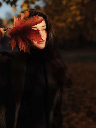 Young beautiful pregnant woman with dark hair in a black tight dress and coat posing on an autumn meadow in the parkの写真素材