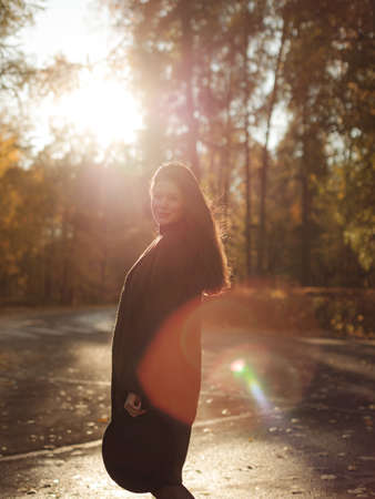 Young beautiful pregnant woman with dark hair in a black tight dress and coat posing on an autumn meadow in the parkの写真素材