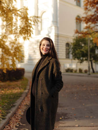 Young beautiful pregnant woman with dark hair in a black tight dress and coat posing on an autumn meadow in the parkの写真素材