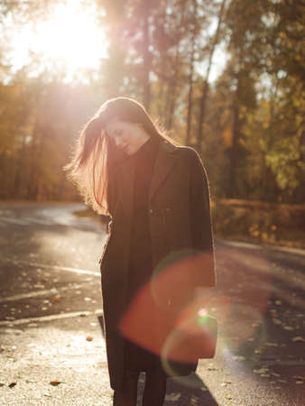 Young beautiful pregnant woman with dark hair in a black tight dress and coat posing on an autumn meadow in the parkの写真素材