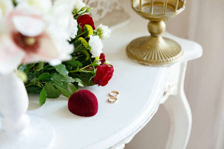 Two wedding rings in white and red gold with a bridal bouquet with red roses