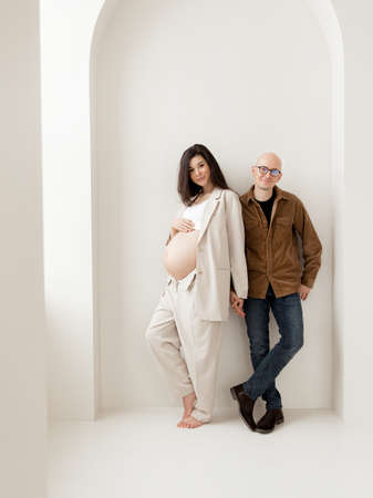 Stylish pregnant brunette in a beige trouser suit and a man in a shirtの写真素材