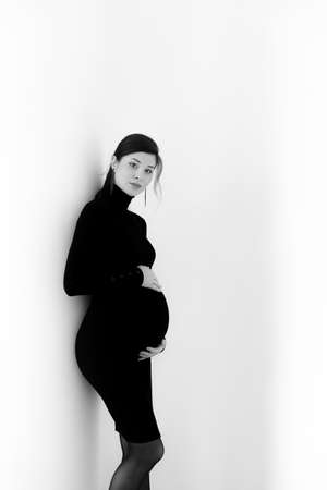 Pregnant brunette in a black dress with a neck on a white backgroundの写真素材