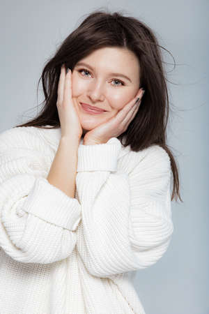 Girl in light jeans and a white oversized sweater on a gray backgroundの写真素材