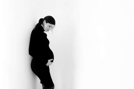 Pregnant brunette in a black dress with a neck on a white background