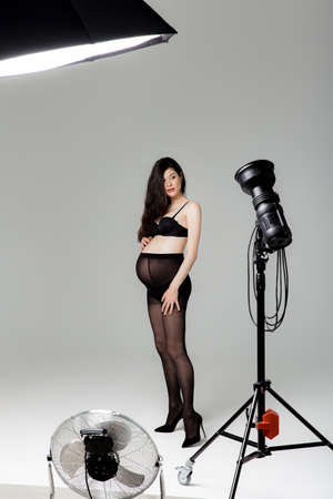 Pregnant brunette girl in pantyhose, bra and shoes in a photo studioの写真素材